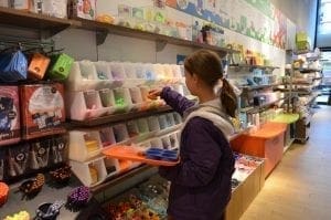 A young girl with brown hair in a purple jacket reaches for candy in a store display.