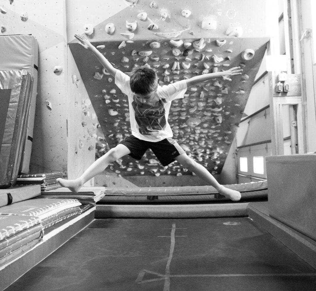 Young person in mid-air with arms and legs extended while climbing an indoor wall.