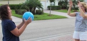 Two people playing catch with a blue textured ball in a suburban setting.