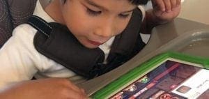 Child wearing a harness looks at a tablet computer.