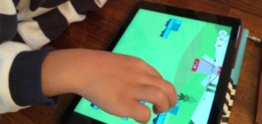 Child's hand touching a tablet screen with a game on it.