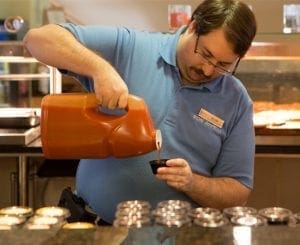 Man in blue polo shirt pouring liquid from a jug into a small container.