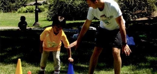 A coach guides a child during an adapted physical education activity outdoors.
