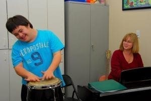 Riley plays a drum while Noreen Donnell watches him.