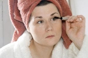 Woman applying mascara with a towel wrapped around her head.