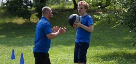 Two people in blue shirts in a grassy area with a ball.