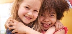 Two young girls hugging and smiling.