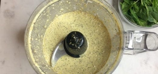 Cashew cream sauce in a food processor with basil in a bowl nearby.