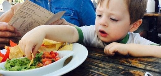 A young boy dips a tortilla chip into guacamole.