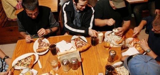 Group of men eating pizza at a wooden table.