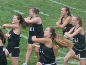 Cheerleaders in black uniforms perform a routine on a grassy field.
