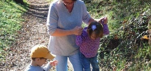 Adult and two children walking on a wooded path.
