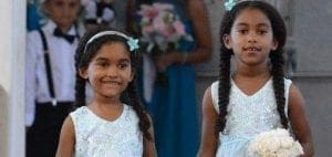 Two young girls in white dresses and blue hair bows.