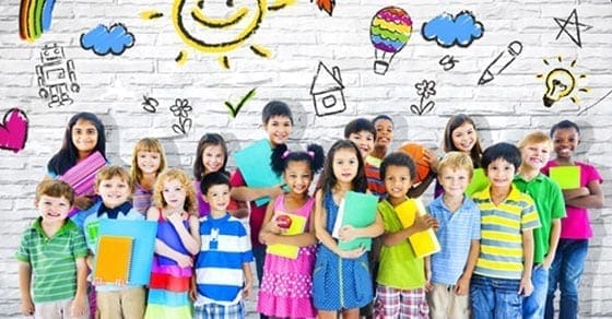 A diverse group of happy children stand in front of a brick wall with colorful drawings of sun, clouds, and school supplies.