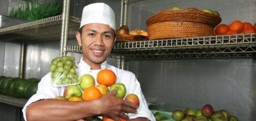 Chef holding a variety of fruits in a kitchen storage area.