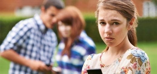 Teenage girl looking distressed while two teenagers whisper in the background.