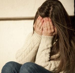 Teenager covering face with hands.