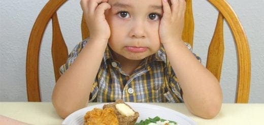 Child with hands on head looking at a plate of food.