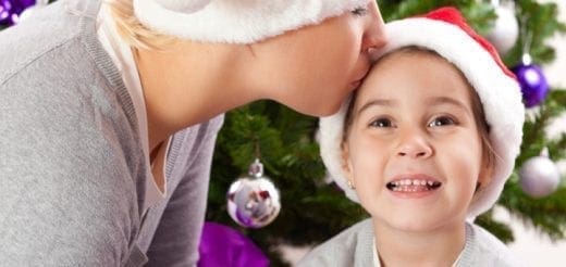 Mother kissing child on forehead near Christmas tree