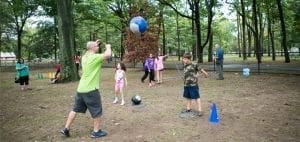 Adults and children play with a large ball in a park setting.
