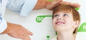 A person measures a boy's height against a wall with height markers.
