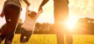 Parents holding hands with a child while walking through a field during sunset.