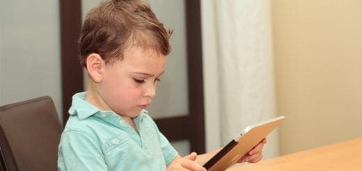 Young boy in a teal collared shirt looking at a tablet computer.