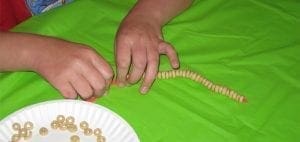 Hands stringing O-shaped cereal onto a string.