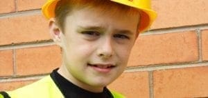 Young boy wearing a yellow hard hat and safety vest.