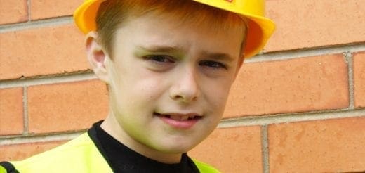 Young boy wearing a yellow hard hat and safety vest.
