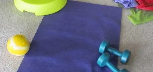 Purple yoga mat on a carpeted floor surrounded by a lime green platform, a yellow ball, two dumbbells, and resistance bands.