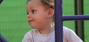 Young child in a white shirt on a playground structure.