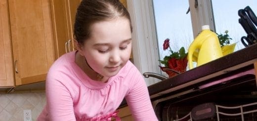 Young girl in pink shirt doing chores in the kitchen.