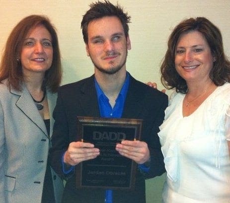 Jordan Obrecht holding a DADD award with two women.