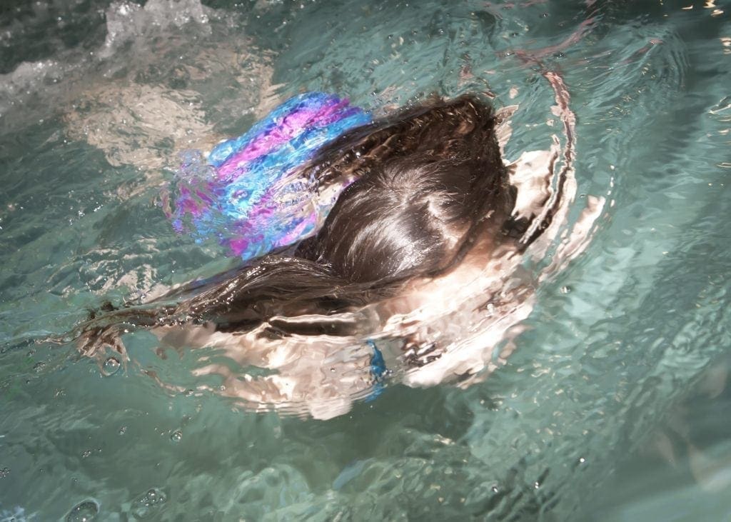 Child swimming in a pool while wearing a personal flotation device.