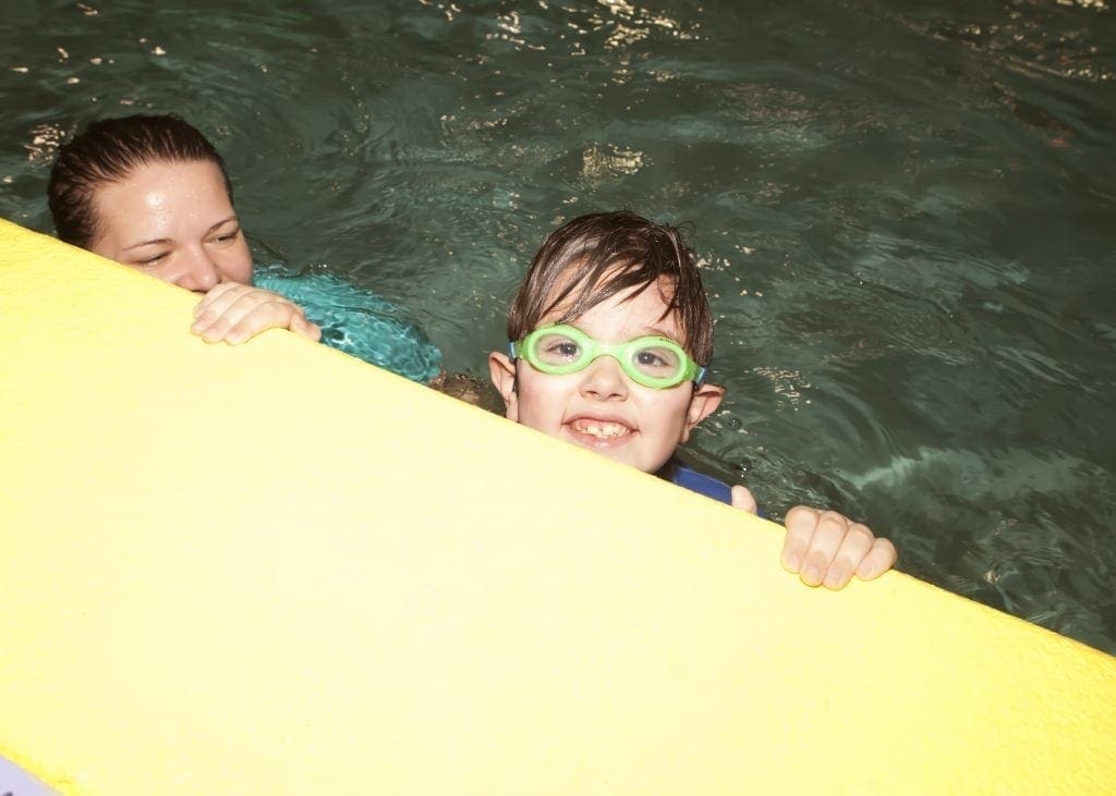 Child with goggles and woman in water behind a yellow float