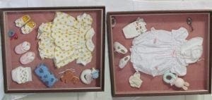 Two shadow boxes display baby clothing and keepsakes.