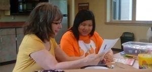 Two women look at a piece of paper together at a table.