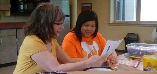Two women look at a piece of paper together at a table.
