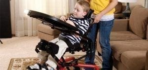 Boy in a standing frame with a person standing behind him.