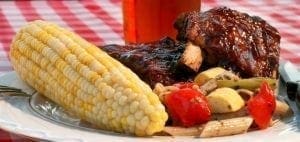 Ribs, corn on the cob, and vegetables on a plate.