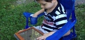 Young child in a blue chair using a tablet outdoors.