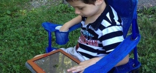 Young child in a blue chair using a tablet outdoors.