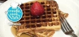 Waffles with syrup and a strawberry, next to a fork.
