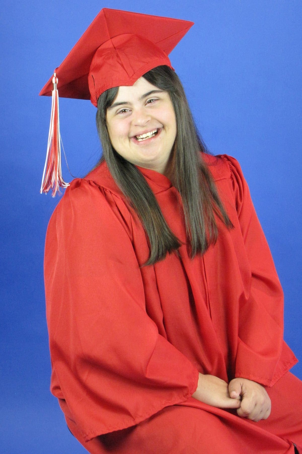 A young woman in a red graduation gown and cap smiles against a blue background.