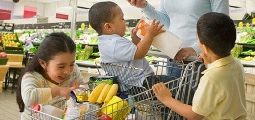 Three children in a grocery store with full shopping carts.