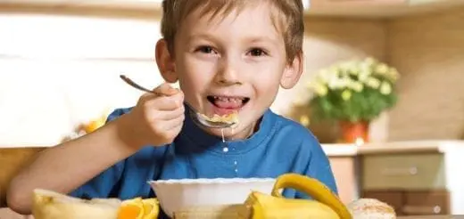 Young boy eating a bowl of cereal with a banana nearby.