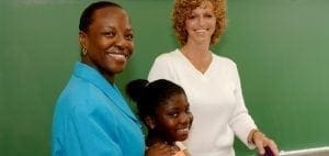 Two women and a child stand in front of a green chalkboard.