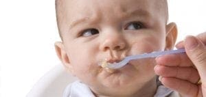 Baby with a spoon of food near its mouth.