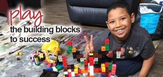 Boy smiling and giving a peace sign near building blocks.
